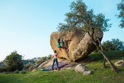 Friends go in for sports in nature, bouldering on rocks, girl climbs a big stone, woman is belayng partner, outdoor recreation, bouldering on the boulders of Lake Bafa