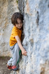 A boy climbs a rock, a little rock climber is training to climb a boulder, a child goes in for sports