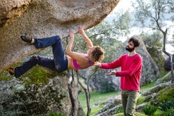 Friends go in for sports in nature, bouldering on rocks, girl climbs a big stone, man is belayng partner, outdoor recreation, bouldering on the boulders of Lake Bafa