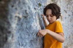 A boy climbs a rock, a little rock climber is training to climb a boulder, a child goes in for sports