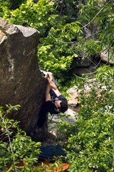 Bouldering on natural terrain, a strong man climbs a boulder, a man goes in for sports in nature, an effort to overcome