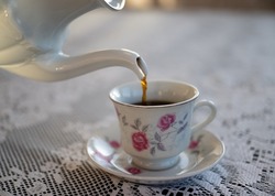 Pour the hot coffee in small white porcelain rose flower cup on a lace cloth