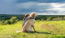 Back view of beautiful little girl hugging loyal dog in nature