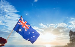Australia flag national hand hold under blue sky at beach with sunlight