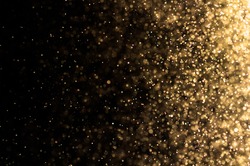 Stardust gold bokeh on black background with flare effect. Glitter golden lighting on dark wall with explosion sparkle on midnight wallpaper concept for Christmas theme or other design.