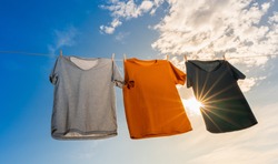 laundry concept of three dry t-shirts hanging on a clothesline with the sun shining in the blue sky