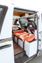 Beautiful bright natural light entering and illuminating an old self converted minivan campervan for van life. The vanlife recreational vehicle has orange seat cushions, stained roof, and van plant.