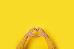 Hands making heart shape, love symbol over yellow background