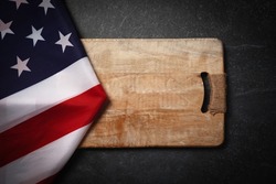 USA flag near empty cutting wood board on dark marble background, layout image, concept of american kitchen