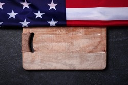 USA flag near empty cutting wood board on dark marble background, concept of american kitchen, layout image