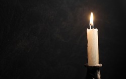 book being illuminated by a burning candle with a black textured background and strong shadows	
