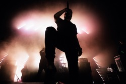 A dark silhouette of a singer on the stage. Good-looking background, bright stag lights. A concert of a famous music band