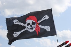Weathered jolly roger flag on windy day, with cloudy sky.