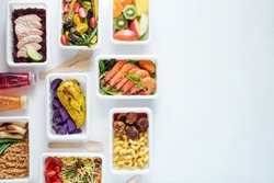 Top view of assorted ready meals over white background with copy space. Prawns, salmon with brown rice, asian noodles, pasta and meatballs, chicken and potato, mushrooms, vegetable and fruit salad. 