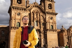 Tourist in the main square of cuzco, holding his camera, with a church in the background.
