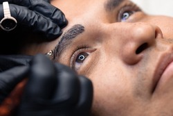 closeup of microblading procedure on man's eyebrows whit his eyes open