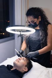 latin woman cosmetologist outlining a man's eyebrows before micropigmentation