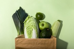 Monochrome photo of a fresh green fruits and vegetables in a paper bag on a green background.Top view.