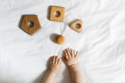 Baby's hands and wooden toys on a white fabric background, early child development