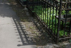 The shadow of the iron cemetery fence on the asphalt path. A sunny summer day. Space for text, background for the design of the poster for the Memorial Day of the dead.