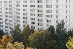 View of wall and windows of white block multi-storey residential building from height. Autumn green and yellow trees, eco-friendly area of Moscow, Russia. Space for text.