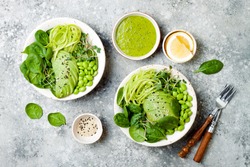 Vegan, detox Buddha bowl with avocado, spinach, micro greens, edamame beans, zucchini noodles and herb green dressing. Top view, grey concrete background
