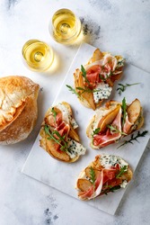 Appetizer crostini, tapas, open faced sandwiches with pear, prosciutto, arugula and blue cheese on white marble board. Delicious snack, appetizers