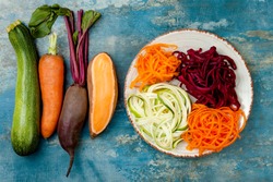 Zucchini, carrot, sweet potato and beetroot noodles on a plate. Top view, overhead. Blue rustic background