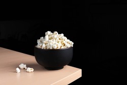 Popcorn table corner wood dark contrast spill movie film theater snack salty sweet bowl plate minimalistic wooden cinema evening copy space dark black white homemade clay crunchy shot photography