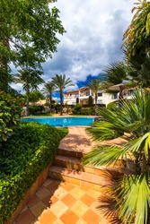 Swimming pool, sun-loungers and palm trees during a warm sunny day, paradise destination for vacations. Backyard swimming pool with garden full of palm trees and flowers. Backyard with swimming pool.