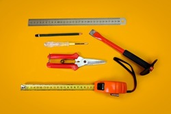 household carpentry tools, tape measure, wire scissors, screwdriver, iron ruler, pencil on an orange background