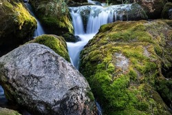 Moss rock , clean rock . two opposite elements together. Flowing water from background shot with long exposure. a river or stream or waterfall.selective focus.