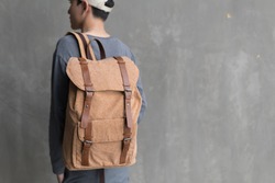 Handsome Asian man with lightbrown ( cork ) canvas backpack smiling standing with cap.