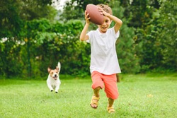 Kid playing American football ready to make touchdown and dog chasing him