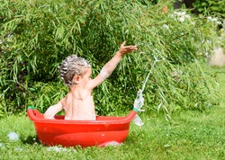 Preschooler boy taking bath outdoors playing with suds foam in washing basin