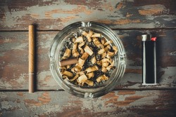 Concept of unhealthy lifestyle, unhealthy breakfast. Flat lay of composition with glass ashtray, cigarette stub and cigarette lighter. Top view, wooden background. High quality photo.