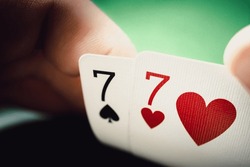 A pair of sevens in a man's hand close up. Seven of hearts and seven of spades, poker background.