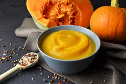 Pumpkin puree with fresh pumpkins and spices in spoon on linen cloth over dark grunge background