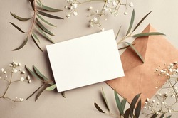 Greeting or invitation card mockup with craft paper envelope, eucalyptus and gypsophila twigs. Card mockup with copy space on beige background.