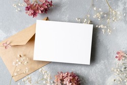 Invitation or greeting card mockup with envelope and flowers decorations. Blank card mockup on grey background.