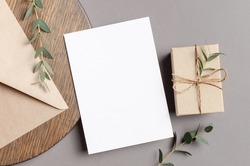 Blank greeting card mockup with gift box and envelope on wooden background