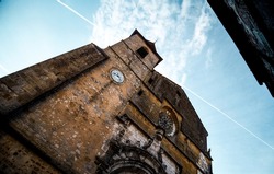 
Low angle photo of a very old French church, Saint Dominique de Monpazier, in Dordogne, Nouvelle -Aquitaine - The sky is blue with some clouds