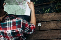 stylish hipster traveler exploring map at sunny forest and lake in the mountains