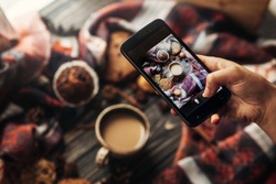 instagram photography blogging workshop concept. hand holding phone taking photo of stylish winter flat lay coffee cookies and spices on wooden rustic background. cozy mood autumn.
