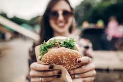 big juicy burger in hand. stylish hipster woman holding yummy cheeseburger. boho girl at street food festival. summertime. summer vacation picnic. space for text