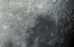 Lunar surface photographed in color. Many terrain formations are visible, such as craters, highlands, lava-flooded areas of the lunar mare, and traces of blowout material from crater formation.