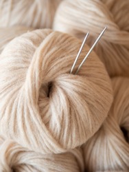 Aesthetic image of beige light, airy yarn skein. Close up view of medium thick blow yarn made of baby alpaca and merino wool. Knitting needles stuck in skein of yarn. Copy space