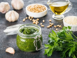 Homemade parsley pesto sauce and ingredients on dark cement background. Close up wiev of parsley pesto in glass jar with ingredients.