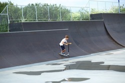 Active ten year old boy riding a scooter in the summer skate park