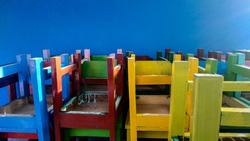 Colorful chairs for school children in the corner of the school building that are placed upside down, chairs with contrasting colors isolated on blue background